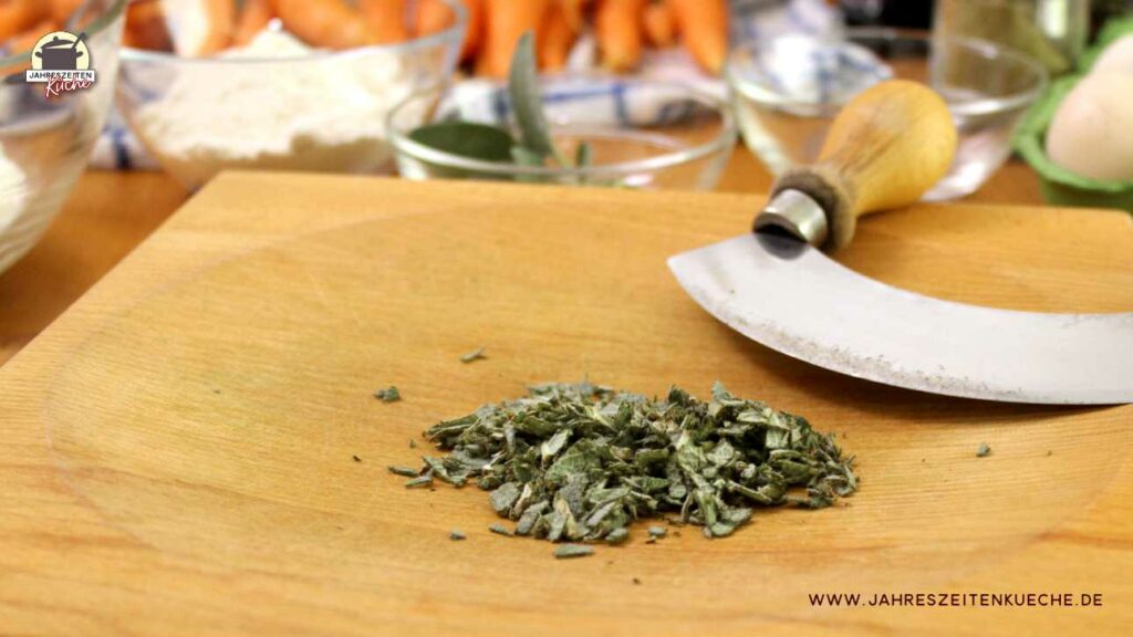 Auf einem Holzbrett liegt gehackter Salbei. Im Hintergrund sind Glasschüsseln mit den Zutaten für den Bremer Teller
