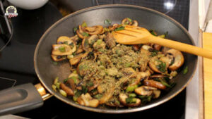 Gedünstete und mit Gewürzen bestreute Champignons und Frühlingszwiebeln in einer Pfannebestreut