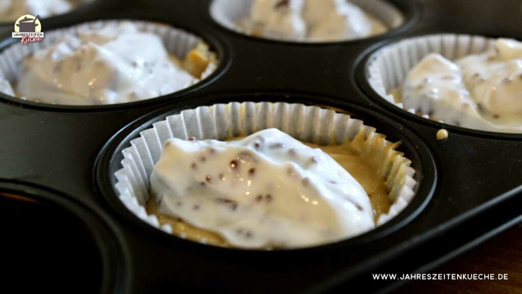 In einer Muffinform sind Papierförmchen mit Teig und Stracciatella-Quark gefüllt