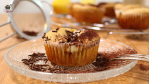 Ein Zitronenmuffin mit Stracciatella-Quark-Füllung steht auf einem Glasteller