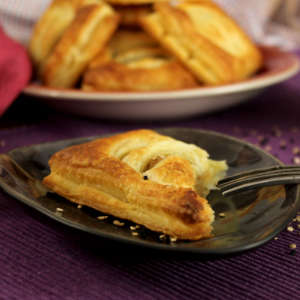 Vor einem Teller mit Blätterteigtasche mit Kartoffelfüllung steht ein kleiner Portionsteller, auf dem eine Blätterteigtasche liegt.
