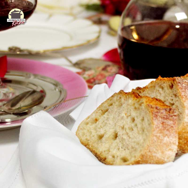 Weißbrotscheiben liegen in einer kleinen Schale. Dahinter steht eine Karaffe mit Rotwein