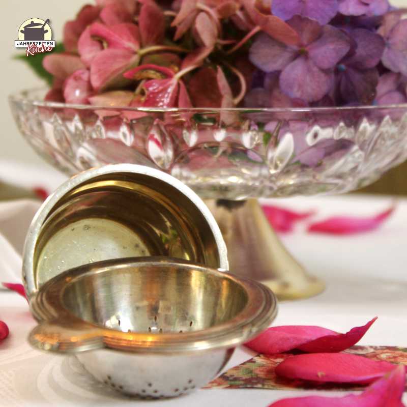 Vor einer Schale mit Hortensien liegt ein silbernes Teesieb