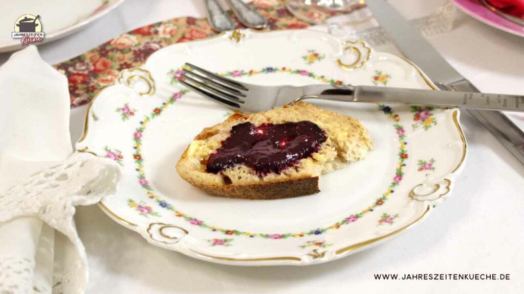 Ein mit Blumen verzierter Teller mit einem Marmeladenbrot und einer Gabel.