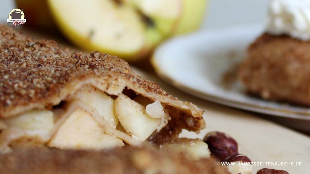 Ein angeschnitter Apfelstrudel im vordergrund, im Hintergrund liegen Äpfel