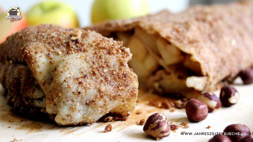 Ein frisch gebackener Apfelstrudel mit Haselnüssen liegt auf einem Holzbrett