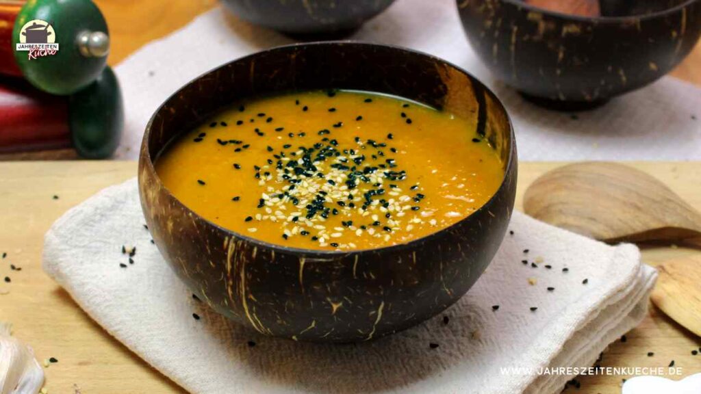 Eine schnelle Kürbissuppe in einer braunen Kokoschale ist mit Sesam und Schwarzkümmel bestreut