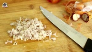 Neben einem Messer liegen klein geschnittene Zwiebeln auf einem Holzbrett