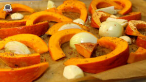 Kürbisspalten, Ziwebeln und Knoblauch liegen auf einem Backblech