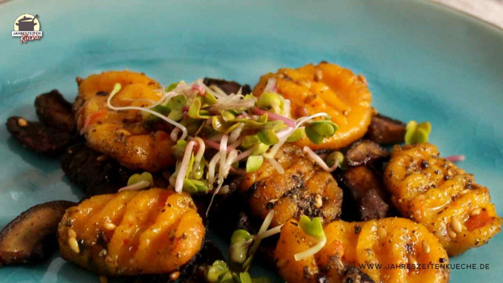 Eine Portion Kürbis-Gnocchi mit gebratenen Champignons und frischen Sprossen ist auf einem türkisfarbenen Teller angerichtet