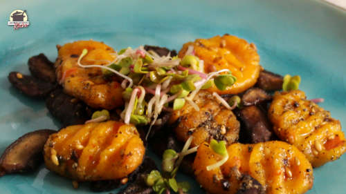 Ein türkisfarbener Teller mit Kürbis-Gnocchi und gebratenen Champignons