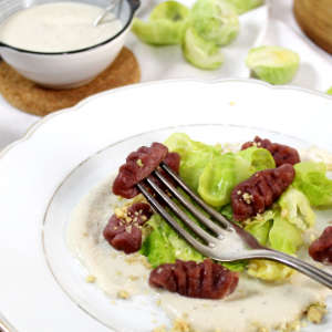 Ein weißer Teller mit Rote Bete-Gnocchi und entblätterten Rosenkohl. Darauf liegt eine silberne Gabel.