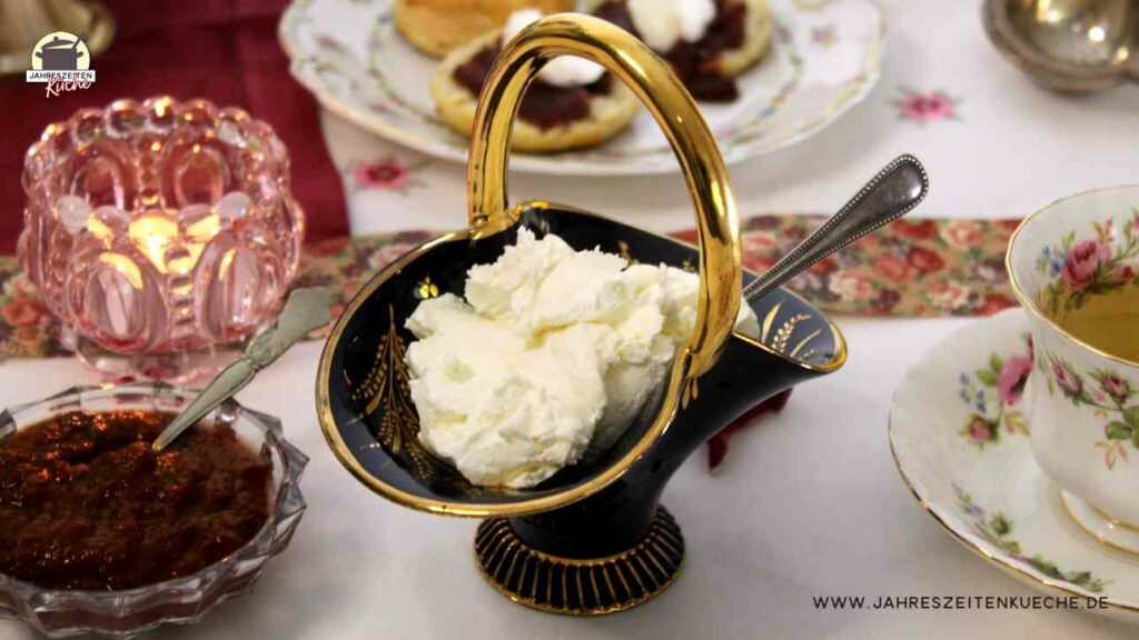 Ein Porzellankörbchen ist mit Clotted Cream gefüllt, Daneben steht eine Tasse Tee