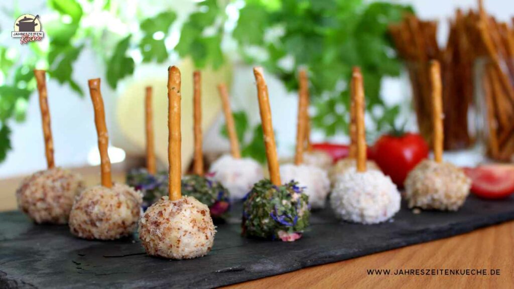 Auf einer Schieferplatte liegen verschiedene Frischkäsekugeln mit Salzstangen