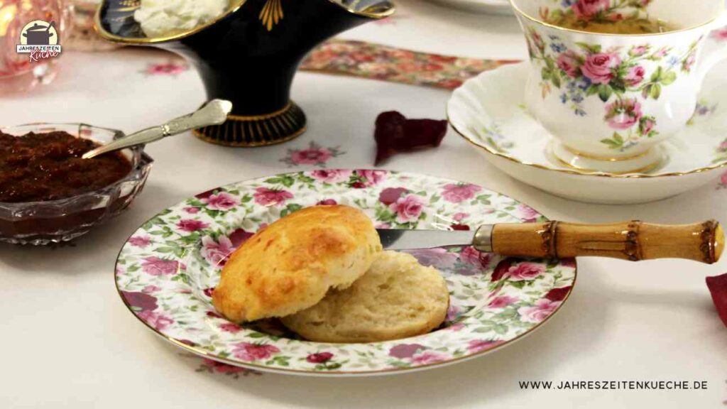 Auf einem Teller mit Rosenmuster liegt ein frischgebackenes Scones und ein Messer mit Holzgriff