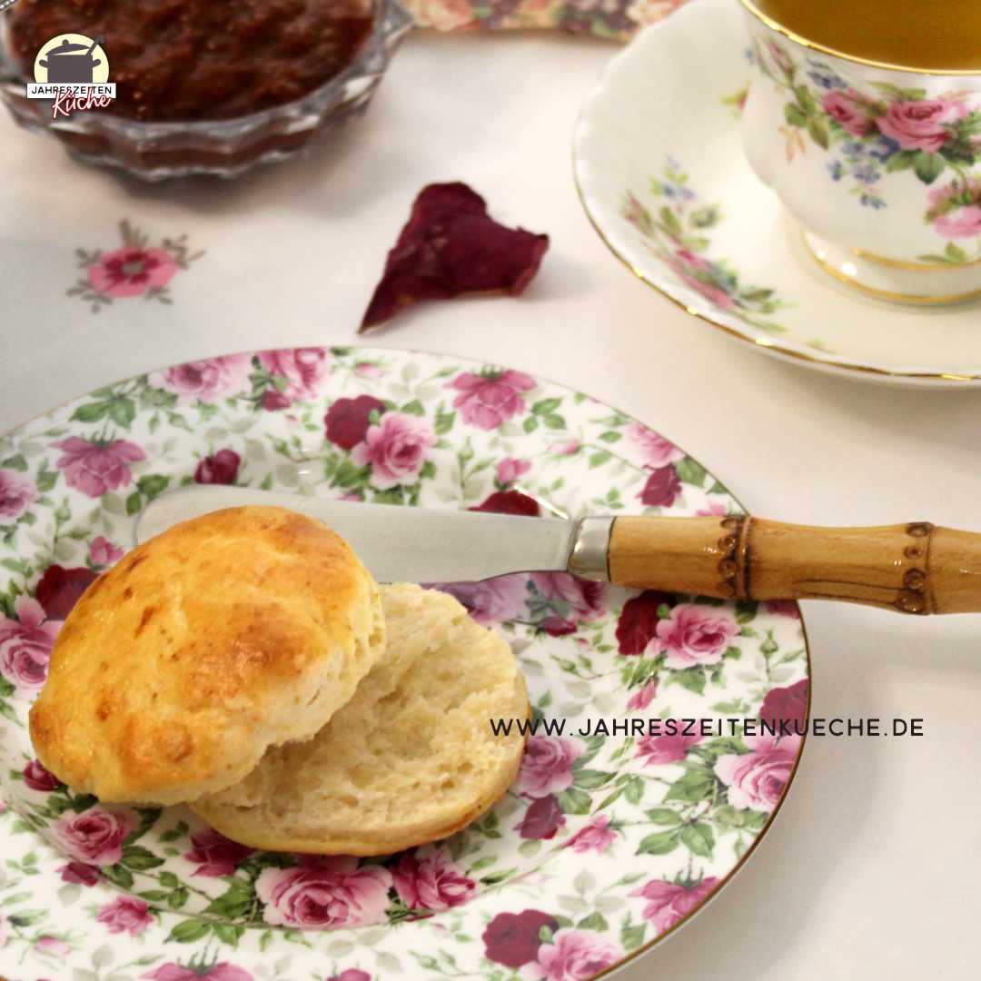 Auf einem Teller mit Rosenmuster liegt ein frischgebackenes Scones und ein Messer mit Holzgriff