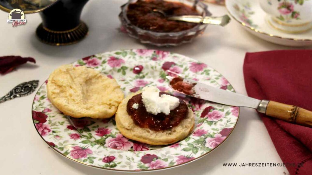 Ein geblümter Teller mit Scones, die mit Erdbeermarmelade und Clotted Cream bestrichen sind