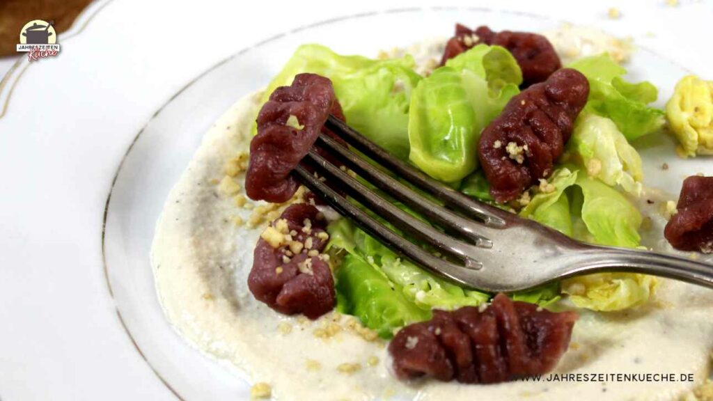 Ein weißer Teller mit Rote Bete-Gnocchi und entblätterten Rosenkohl. Darauf liegt eine silberne Gabel.