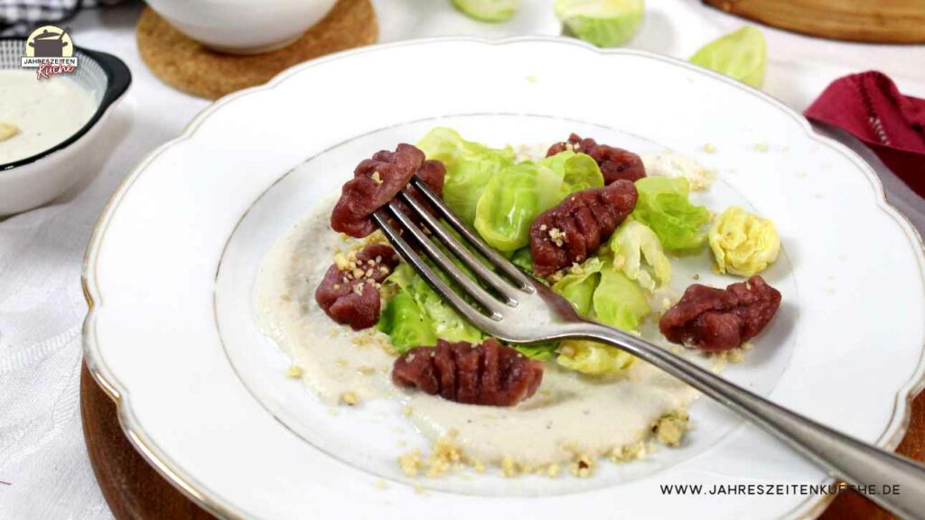 Ein weißer Teller mit Rote Bete-Gnocchi und entblätterten Rosenkohl. Darauf liegt eine silberne Gabel.
