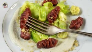 Ein weißer Teller mit Rote Bete-Gnocchi und entblätterten Rosenkohl. Darauf liegt eine silberne Gabel.