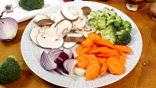 Geschnittene Champignons, Karotten, Brokkoli und Zwiebeln auf einem Teller.