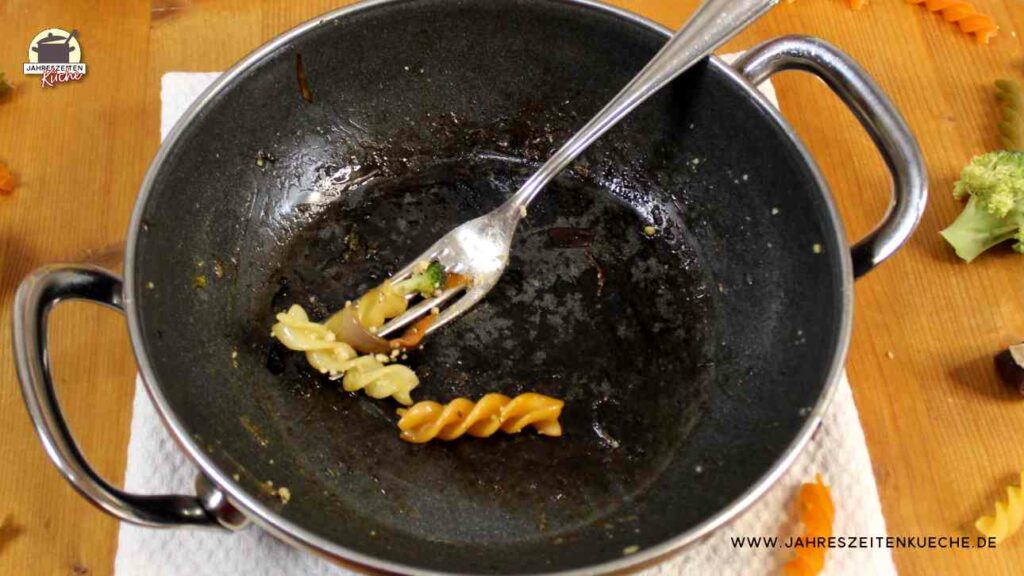 In einer leeren Pfanne liegt eine silberne Gabel und zwei bunte Spirelli-Nudeln