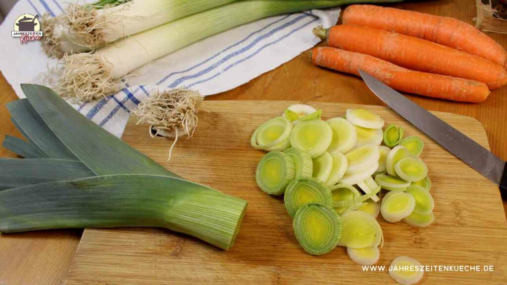 Geschnitter Lauch liegt auf einem Holzbrett. Daneben lieben Karotten