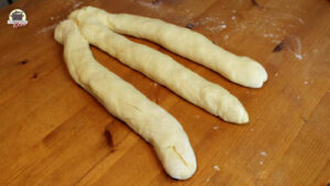 3 Hefeteigrollen zum Flechten liegen auf einem Holztisch