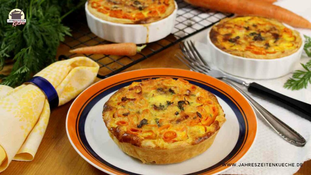 Teller mit einer Karotten-Quiche. Im Hintergrund sind zwei weitere Mini-Quiche in einer Keramikform