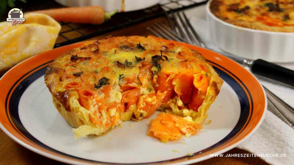 Karotten-Quiche auf einem Teller, von der schon ein Stück fehlt.