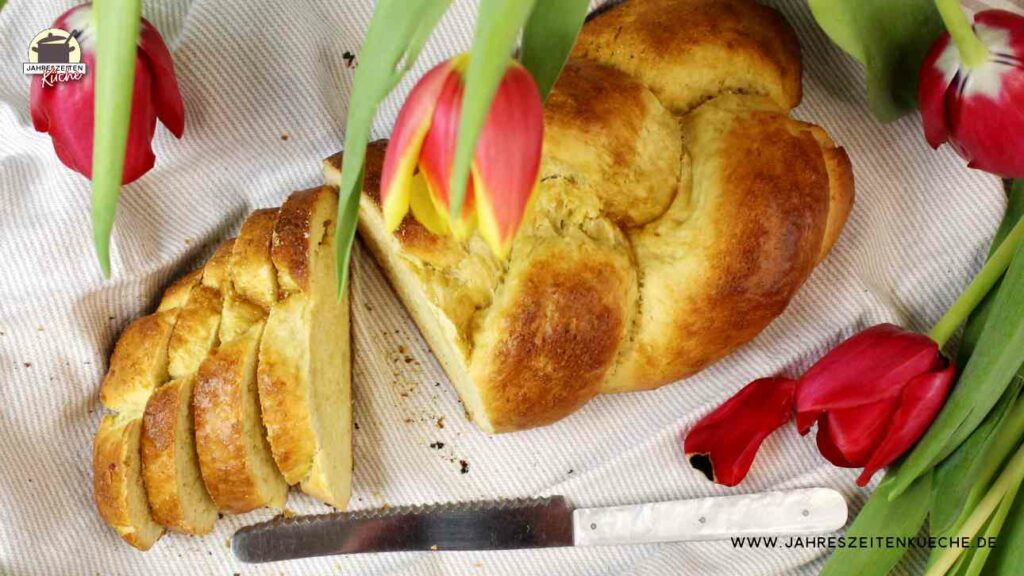 In der Draufsicht ist ein Hefezopf zu sehen, von dem vier Scheiben abgeschnitten wurden. Darüber hängen rot-gelbe Tulpen