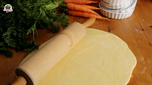 Ausgerollter Quichteig auf einem Holztisch mit Kuchenrolle