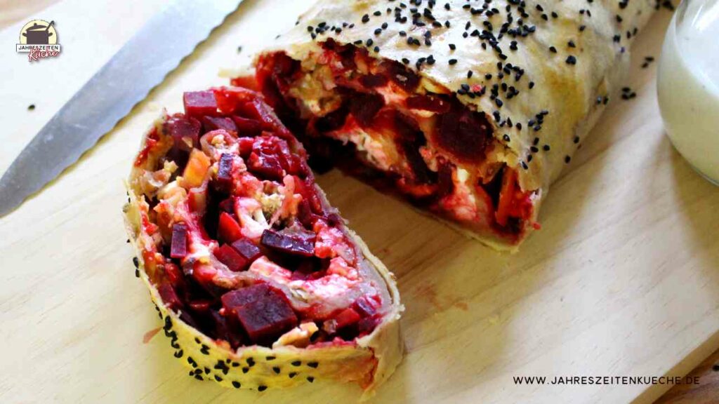 Ein Rote-Bete-Strudel liegt auf einem Holzbrett. Ein Stück ist davon abgeschnitten